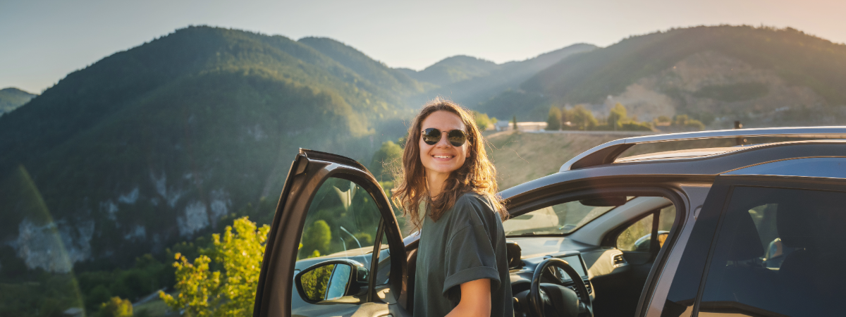 young girl getting out of her car in front of an overlook with mountains in the background